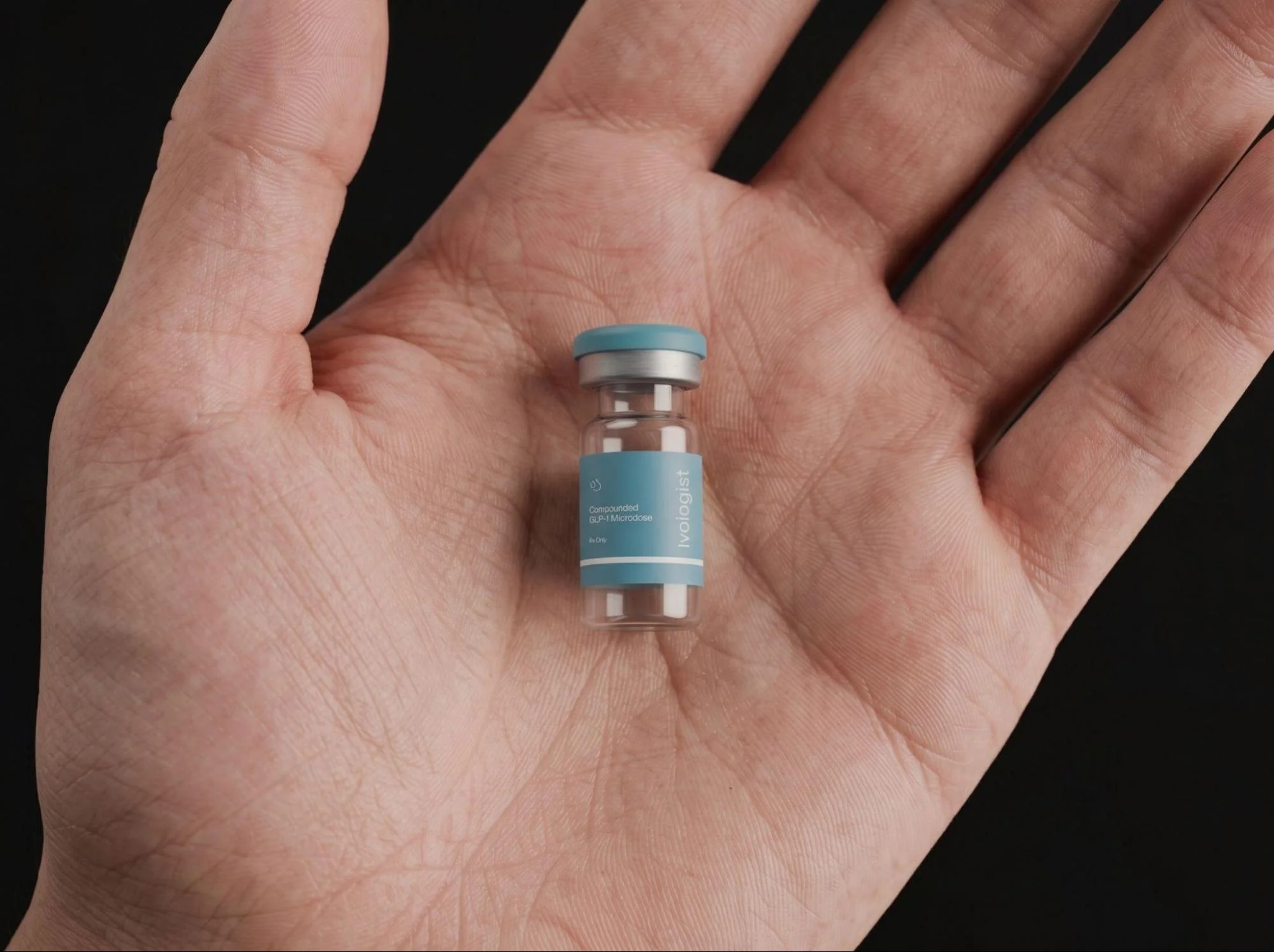 Small semaglutide vial resting in the center of an open hand against a dark background